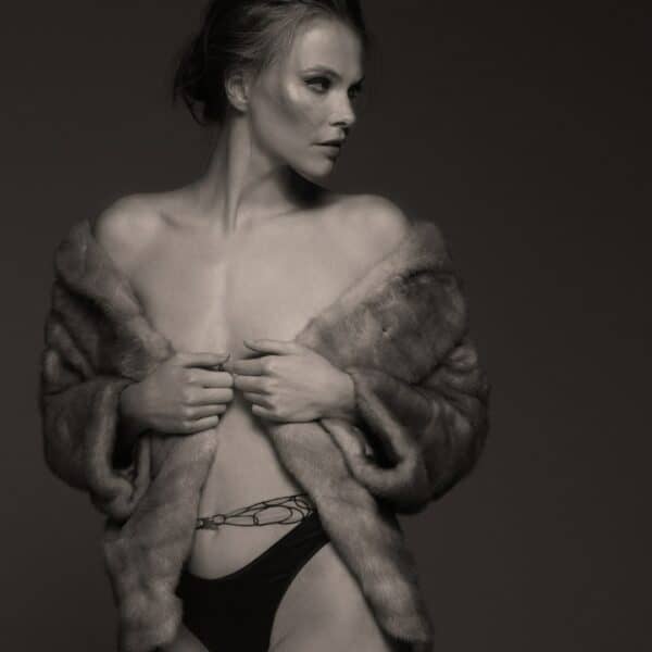 Black and white photograph of a model wearing Valnue's Aria Odyssey Brazilian thong with a coat.