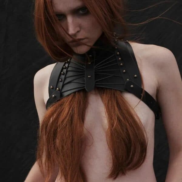 Fond noir de face d'une femme portant un haut Una burke en cuir noir, les cheveux devant la poitrine.