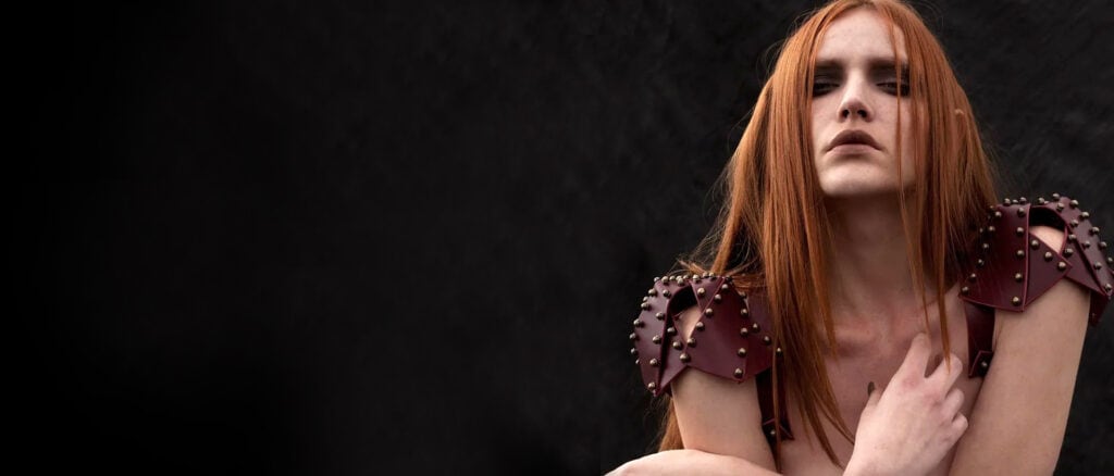 Rückenansicht einer Frau mit roten Lederschulterpolstern auf einem schwarzen Hintergrund von Una Burke.