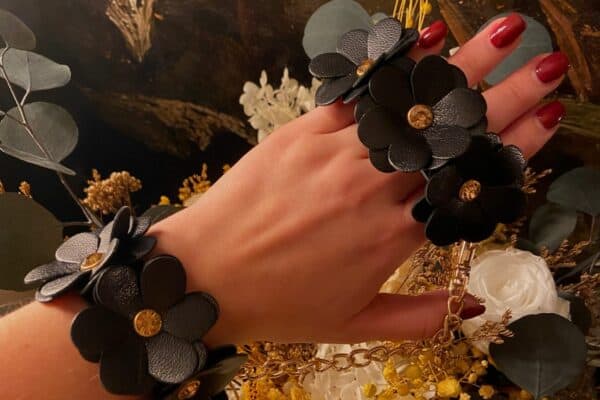Hand, die die beiden Handschellen aus schwarzem Leder im Blumendesign trägt.