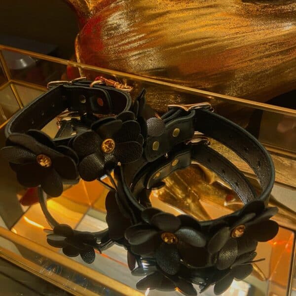Schwarze Lederhandschellen im Blumendesign, die in einer Spiegelaufbewahrung liegen, von oben gesehen.