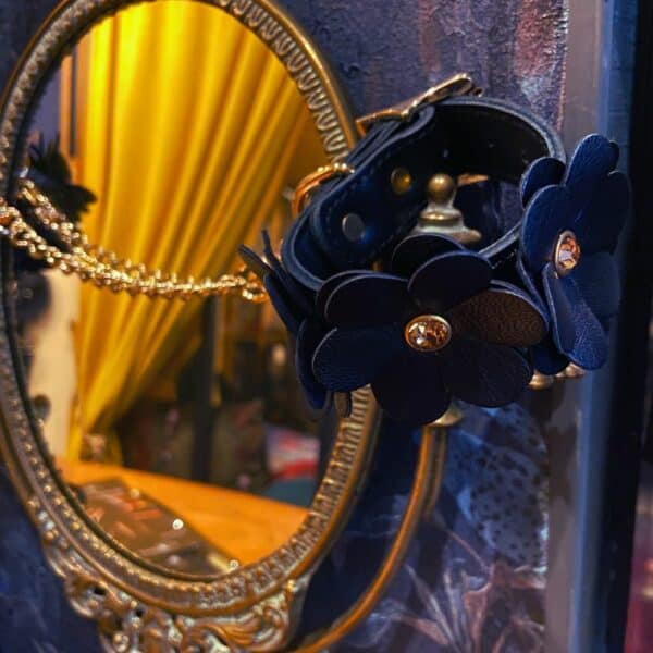 Collier et laisse en cuir au design fleur posés sur un miroir contre un mur.