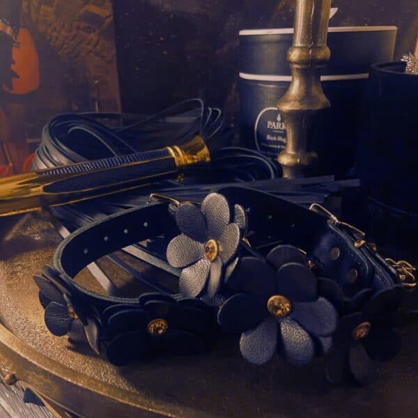 Handschellen aus schwarzem Leder im Blumendesign liegen auf einem Holztisch.