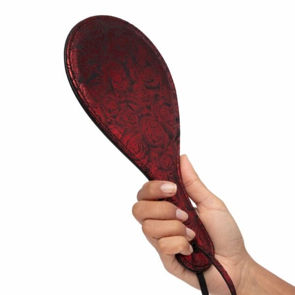 Mano sujetando una pala con tela de raso con estampado de rosas rojas