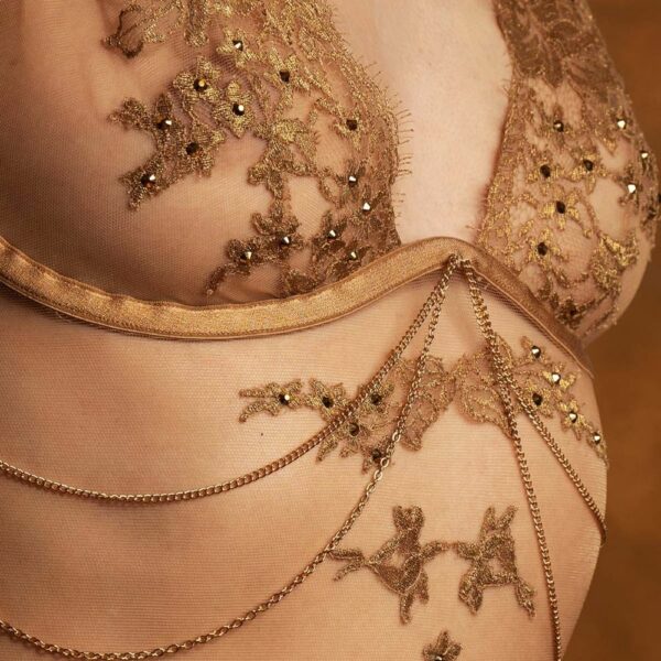 Detail einer 3/4 Frau, die einen fleischfarbenen Body mit goldenen Stickereien trägt.