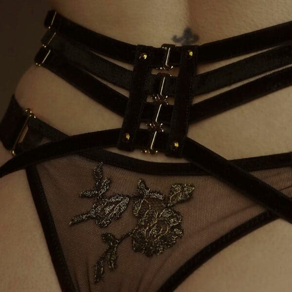 Detail einer Frau mit Rückenansicht, die einen Netzstring und Strapsgürtel mit elastischen Samtbändern in der Farbe Schwarz trägt.