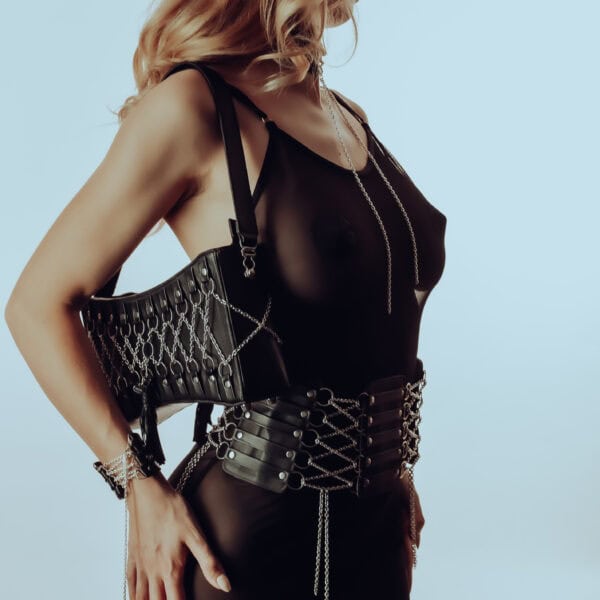 Ceinture corset en cuir et acier inoxydable avec fermeture ajustable, chaîne amovible. Choker en cuir d’agneau avec anneaux en argent sterling. Sac à main en cuir avec design corset argenté, pompom en cuir, intérieur en daim violet.