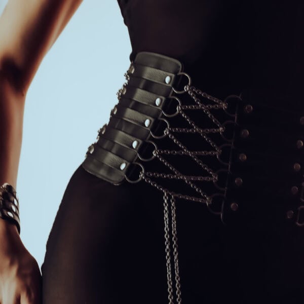 Ceinture corset en cuir et chaînes en acier inoxydable, doublée de daim pour le confort. Ajustable avec fermeture corsetée. Portée avec ou sans attache chaîne porte-jarretelles. Modèle sur commande.