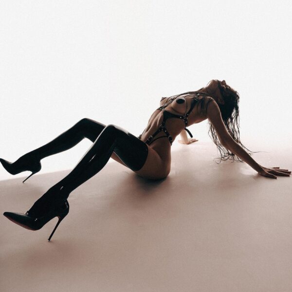 Женщина в черном кожаном жгуте ORA от ANOESES, BDSM-комплект с цепями и металлическими деталями.