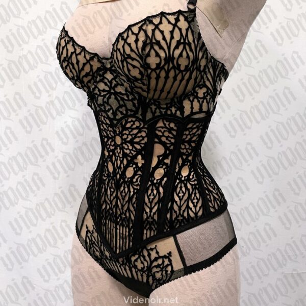 Corset underbust gothique en tulle nude orné de velours noir, avec baleines acier et doublure en velours. Inspiré des formes gothiques. Silhouette structurée et confort assurés.