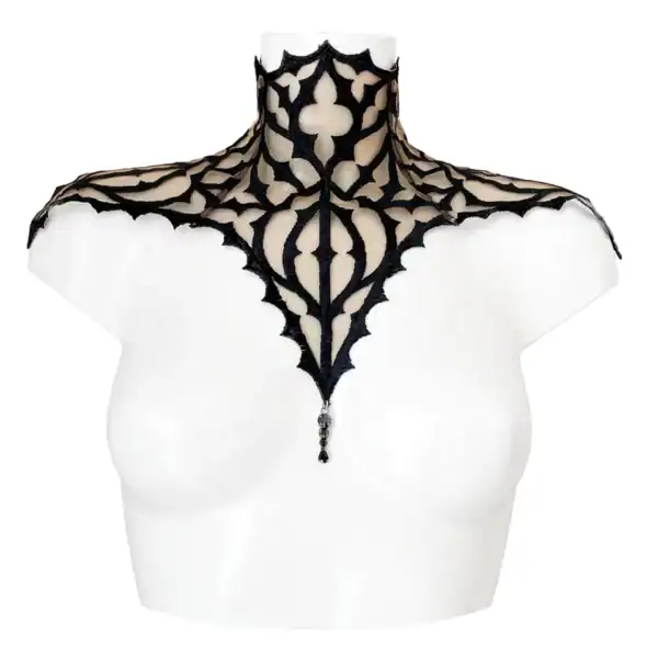 Plastron gothique brodé noir sur tulle nude, orné d’un pendentif central. Forme montante couvrant cou et épaules. Fermeture réglable par ruban façon corset au dos.