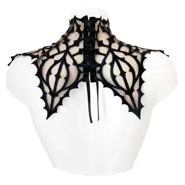 Plastrón gótico bordado en negro sobre tul nude, adornado con un colgante central. Forma ascendente que cubre cuello y hombros. Cierre de lazo tipo corsé ajustable en la espalda.