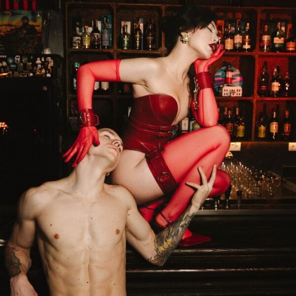 Daelos Korsett, Astrea String, Magnus Oberschenkelzwang und Handschellen aus rotem, vollnarbigem Leder mit Metallbeschlägen, handgefertigte RE:STRICT Bondage-Kreationen.