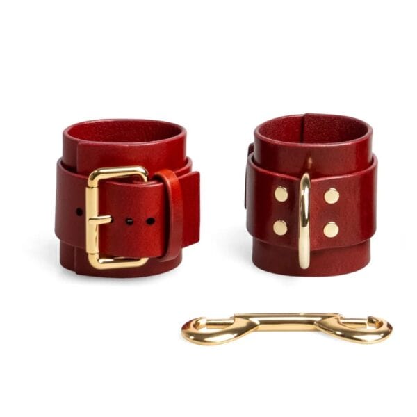 Rote, verstellbare Lederhandschellen mit D-Ring und goldenen Metallbändern. Minimalistische, handgefertigte Bondage-Kreation von RE:STRICT.