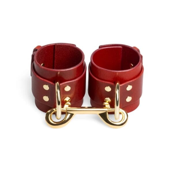 Rote, verstellbare Lederhandschellen mit D-Ring und goldenen Metallbändern. Minimalistische, handgefertigte Bondage-Kreation von RE:STRICT.